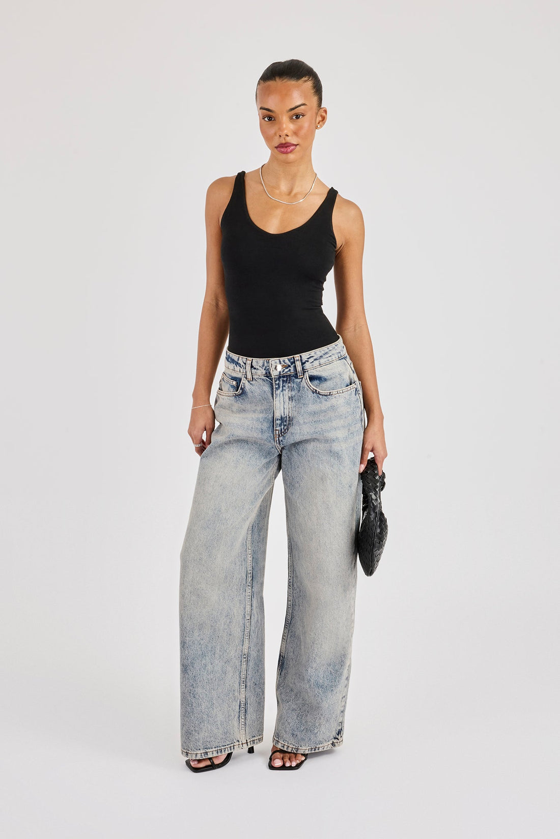 Fitted black scoop-neck tank tucked into pale baggy jeans, with black narrow-strap heels and a black woven clutch